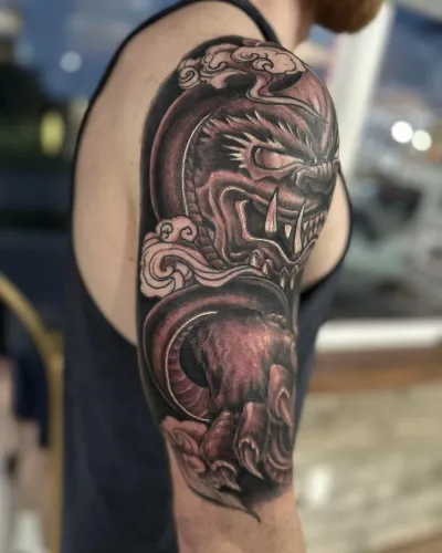 Ornamental black and grey dragon half sleeve wrapping the upper arm — by Adam Crane at Ministry Ink
