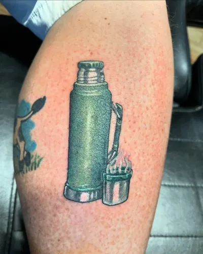 Colour vintage thermos flask and paint tins tattooed on an upper arm — by Adam Crane at Ministry Ink