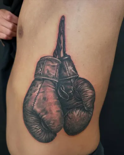 Black and grey boxing gloves hanging from their laces, on the ribs — by Adam Crane at Ministry Ink