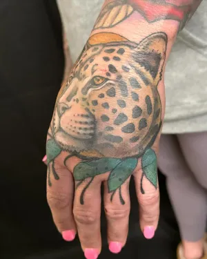 Colour leopard face tattooed across the back of a hand — by Adam Crane