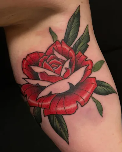 Neo-traditional red rose with green leaves on an upper arm — by Adam Crane at Ministry Ink