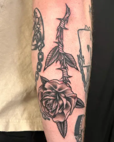 American traditional dagger through a rose on a forearm — by Chay Menke at Ministry Ink