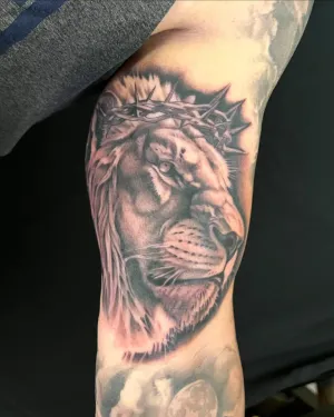 Black and grey lion wearing a crown of thorns on an inner arm — by Chay Menke