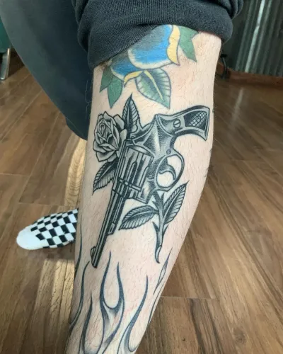 American traditional revolver and roses tattooed down a shin — by Chay Menke at Ministry Ink