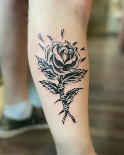Black and grey rose with crossed stems on a calf — by Chay Menke at Ministry Ink