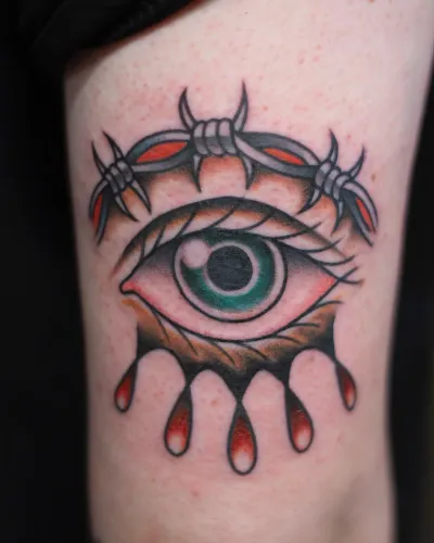 American traditional eye with barbed wire and falling teardrops on a thigh — by Chay Menke at Ministry Ink