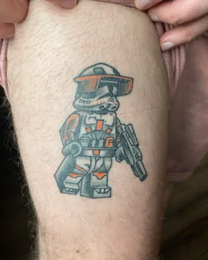 Colour armoured toy soldier figure tattooed on a thigh — by Chay Menke