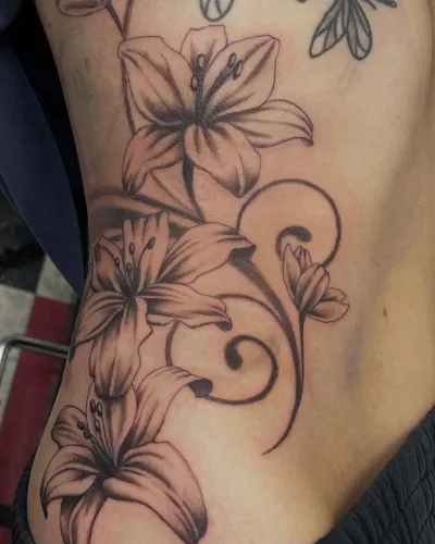 Fine line lilies and trailing vines across the ribs — by Gabriel Gonzalez at Ministry Ink