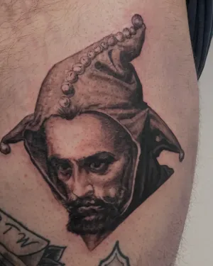 Black and grey portrait of a bearded jester on a thigh — by Gabriel Gonzalez