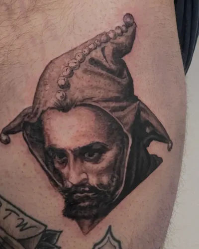 Black and grey portrait of a bearded jester on a thigh — by Gabriel Gonzalez at Ministry Ink
