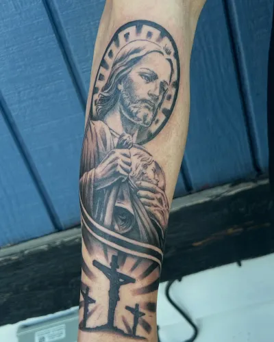 Black and grey religious forearm sleeve with a saint and a cross — by Gabriel Gonzalez at Ministry Ink